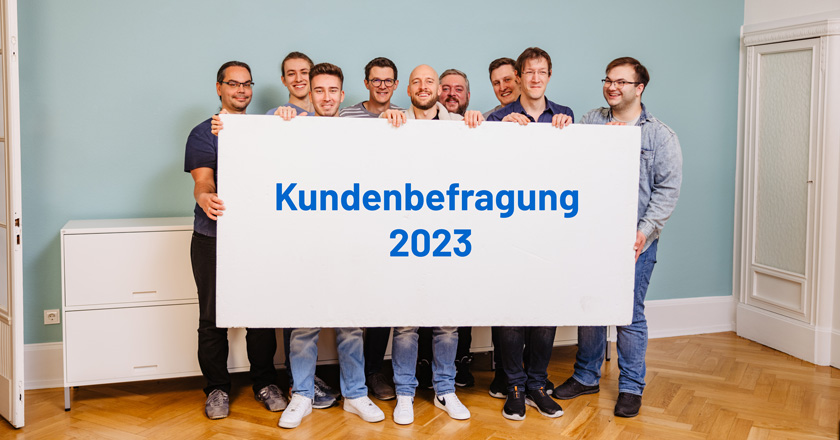 Mitarbeiter von roXtra halten ein Schild mit der Beschriftung "Kundenbefragung 2023" hoch